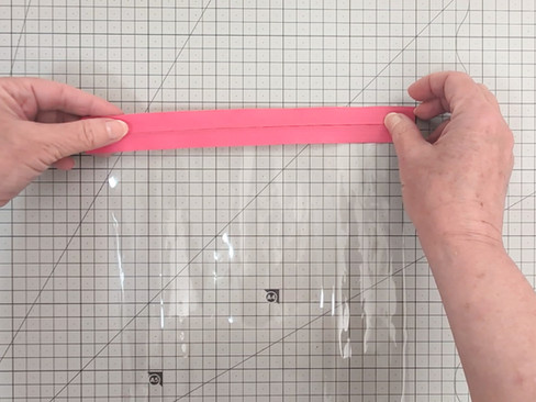 A person's hands holding a pink zipper on some clear vinyl.