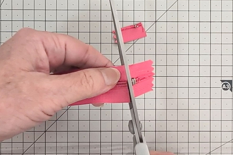 Hand cutting a pink zipper with scissors on a gridded cutting mat.
