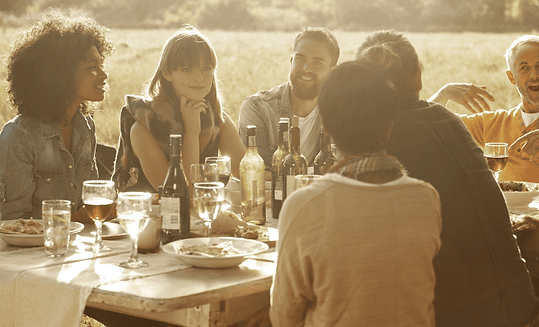 Een groep mensen die buiten gezellig aan een picknicktafel praten en borrelen met elkaar.p
