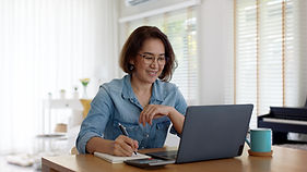 Smiling woman taking notes at her laptop during an online session at home