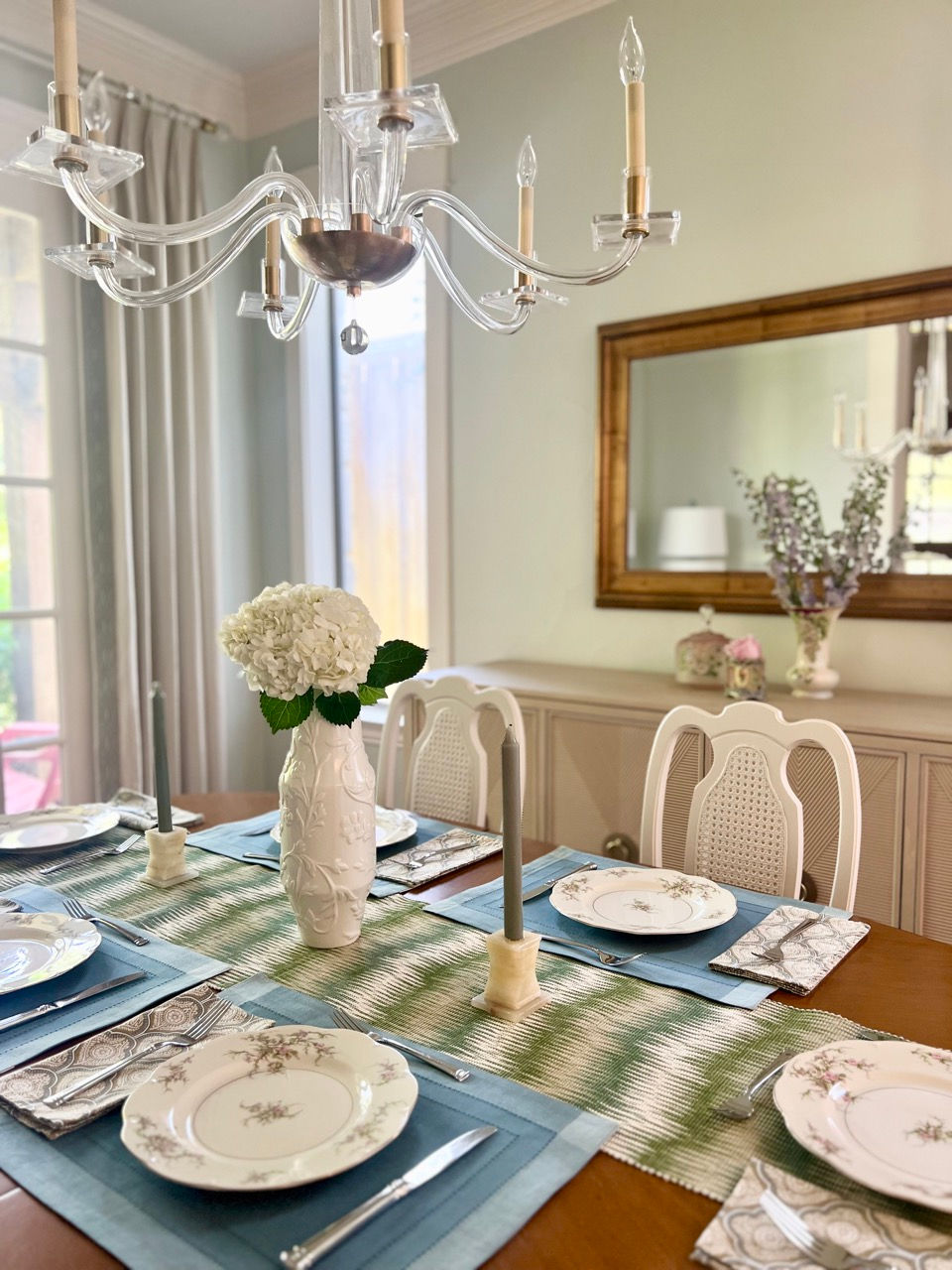 Elegant dining room with light green walls, transitional crystal chandelier, china table setting.