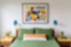Modern guest room with graphic cowboy art, green bedding, yellow trays and blue sconces in mid-century style.