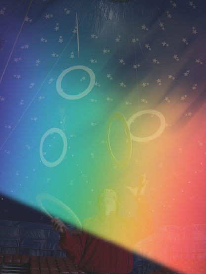 Juggler in a circus tent tosses glowing rings under rainbow light, with starry ceiling and stage lights around them.
