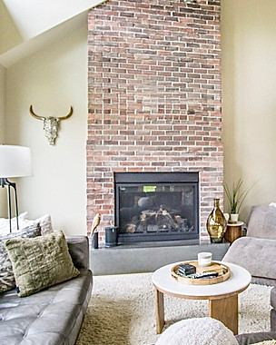 Staged living room with a brick fireplace, leather sofa and round coffee table