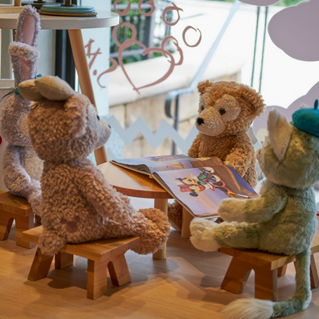 Stuffed toys seating around a table, reading a book, pretend play