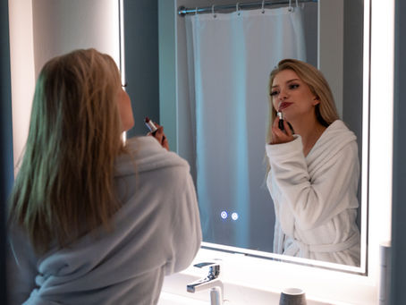 Woman in a plush bathrobe applying lipstick in the mirror, exuding effortless glamour