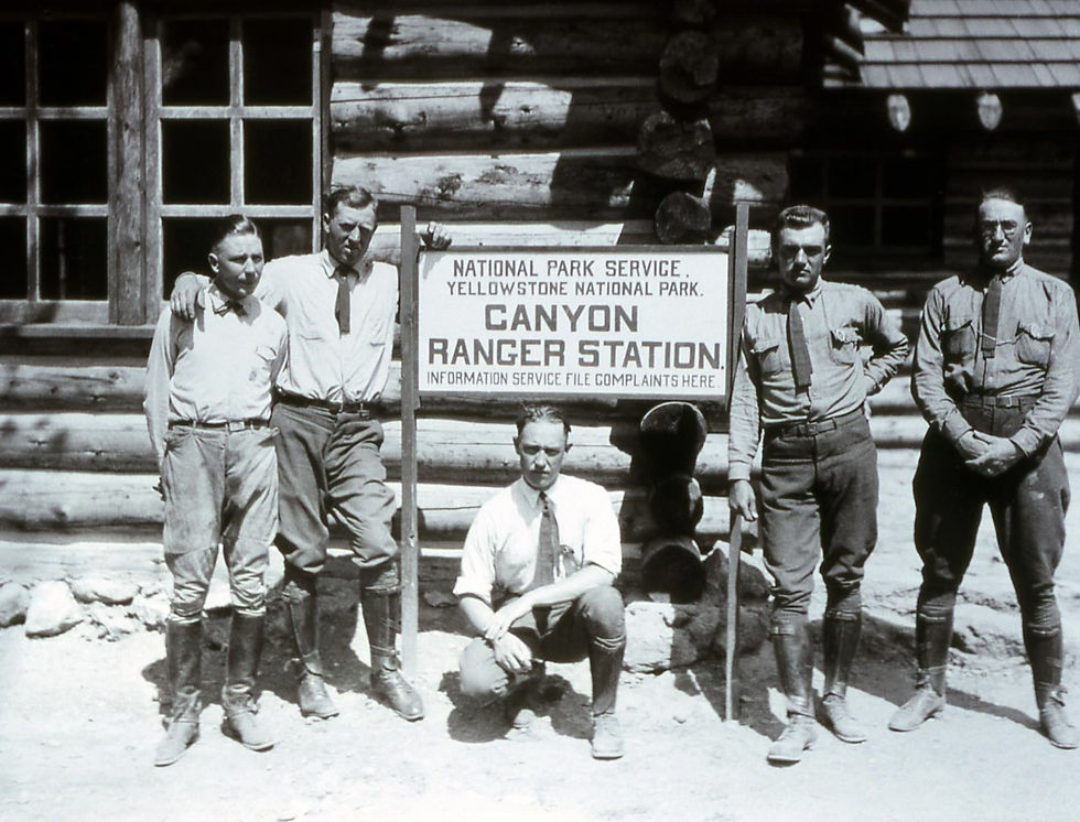 Five men in early twentieth century National Park Service uniforms pose in front of a log cabin structure next to a sign that reads "Canyon Ranger Station."