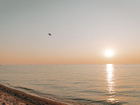 A serene sunset over the ocean with a parasailer gliding through the rosy sky, casting reflections on the tranquil waters below.