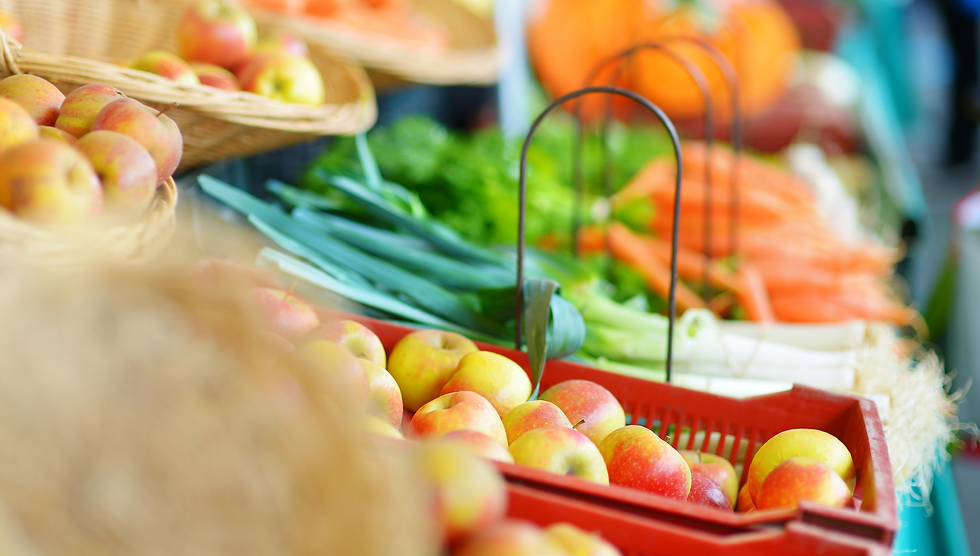 Colorful apples in red crates and baskets at a farmers market, with leeks and other vegetables in a bright, blurred background.