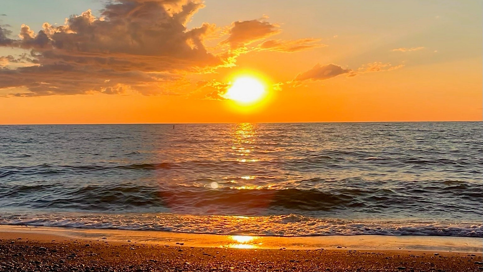 Golden sunset over calm lake waves and pebbled beach, with orange sky and glowing clouds.