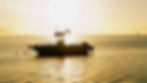 Silhouetted boat YUHMINE III on calm golden water at sunset, with bright sky and reflections on the sea.