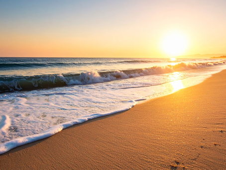 Sunset over a sandy beach with waves crashing gently. The sky is orange and pink, reflecting on the calm sea, creating a serene atmosphere.