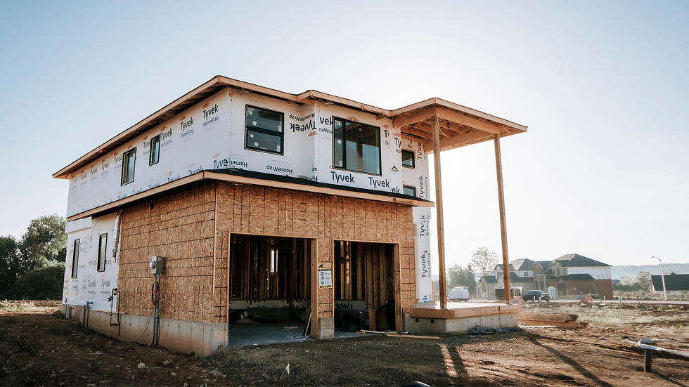 Two-story house under construction with Tyvek wrap and exposed wood framing in a sunny suburban lot, no people visible.