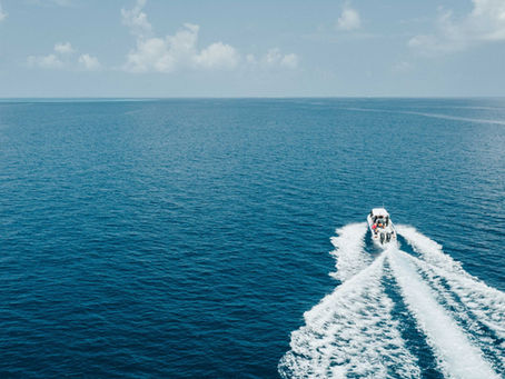 Speedboat speeds across a blue lake, leaving a white wake under a cloudy sky.