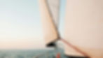 Close-up of white sailboat sails on calm lake at sunrise, with metal railing and soft pastel sky, tranquil mood