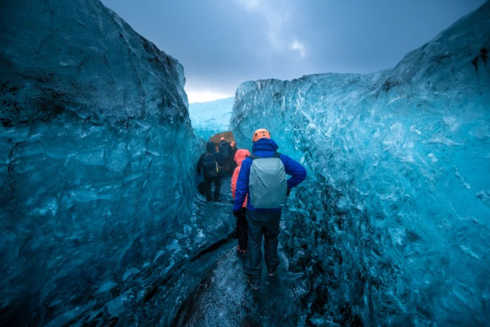 A group of tourists on a ice cave day trip in Iceland, passing through clear, blue glacier