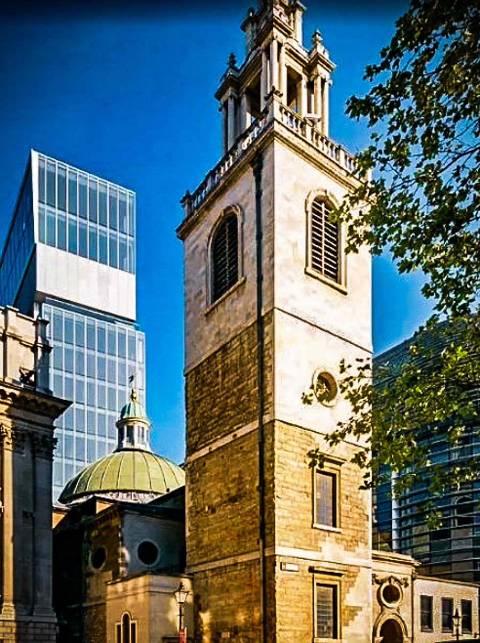 Tour d’église en pierre au centre de gratte-ciel modernes, sous ciel bleu, avec feuillage au premier plan.