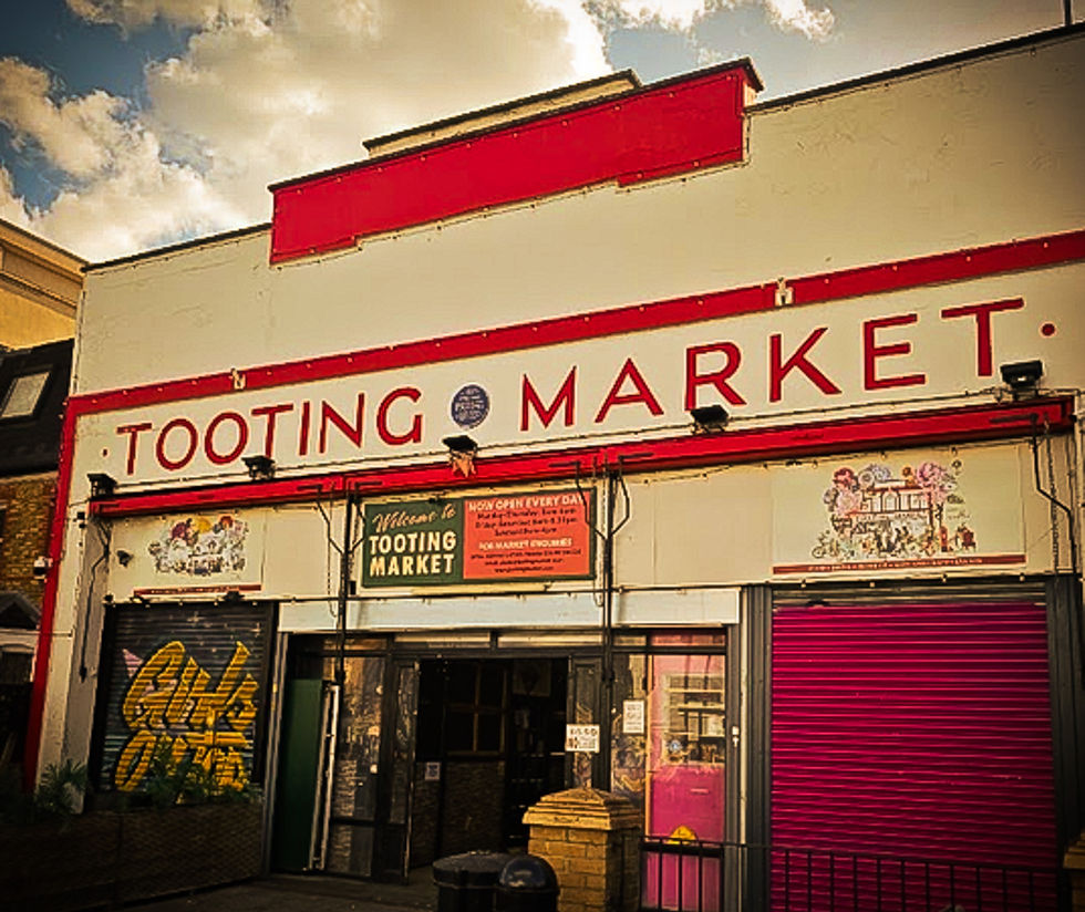 Façade du Tooting Market, grande enseigne rouge sous un ciel nuageux; rideaux fermés et ambiance urbaine.