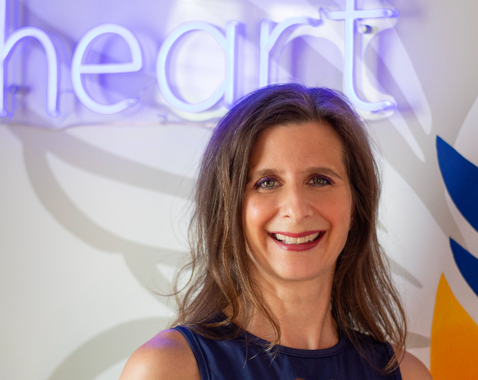 Portrait of Jenny Haddle, founder of Find Your Fierce Heart, smiling in front of a vibrant neon sign.