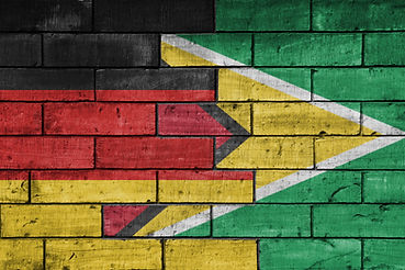 colourful painted big national flag of germany and flag of guyana on a massive old brick w