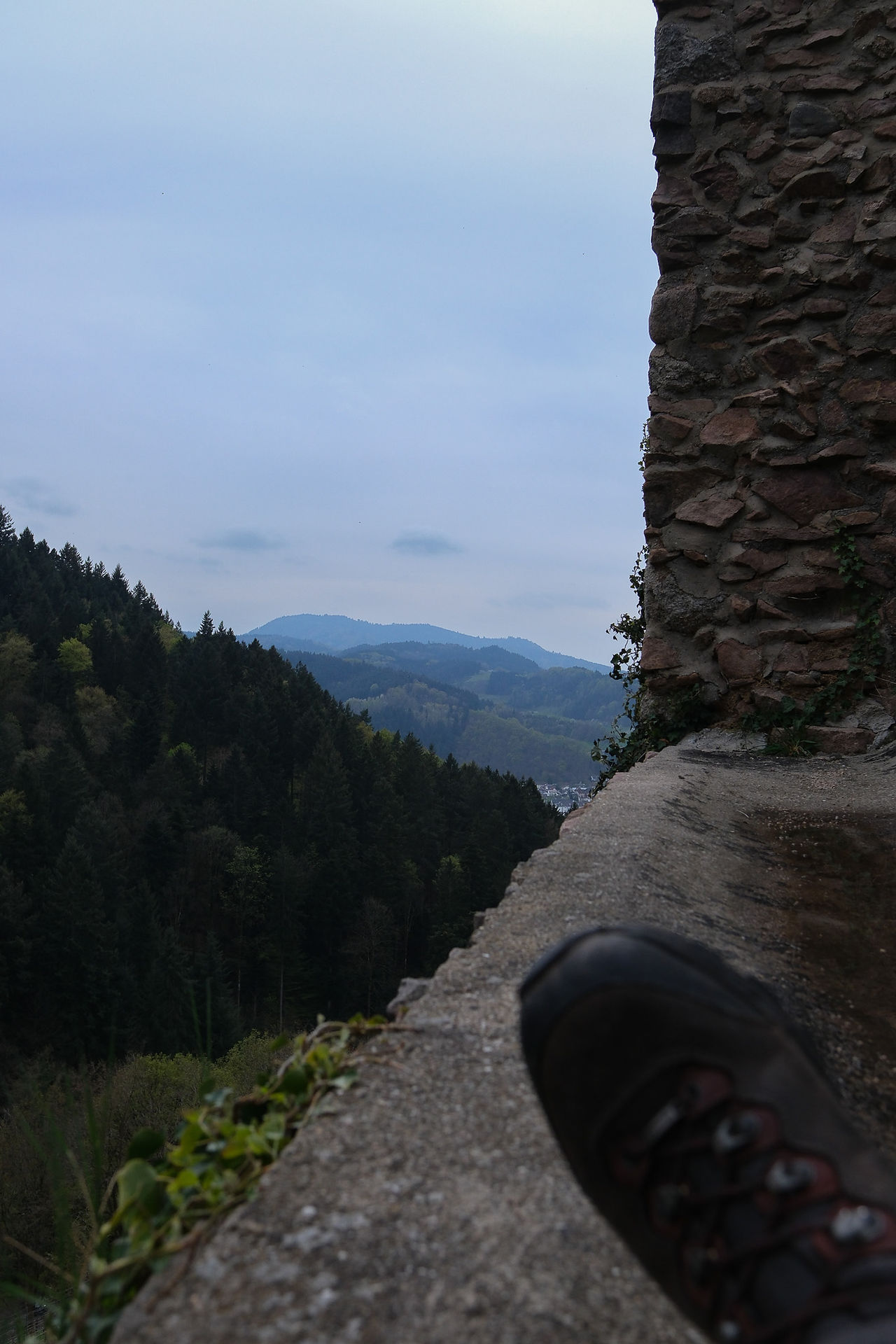 Ein Wanderschuh der auf der Mauerliegt. Berge im Hintergrund
