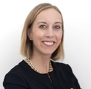 Smiling woman with short blond hair, wearing a black top and gold chain necklace, against a plain white background. Elegant and professional mood.