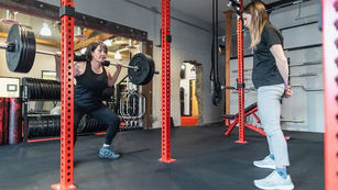 A client performing a squat by the guidance of a strength coach