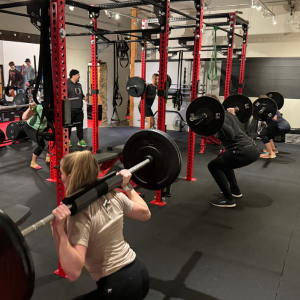 Runners performing barbell squats during a strength training class at Zenith Performance and Wellness, focused on building power and control
