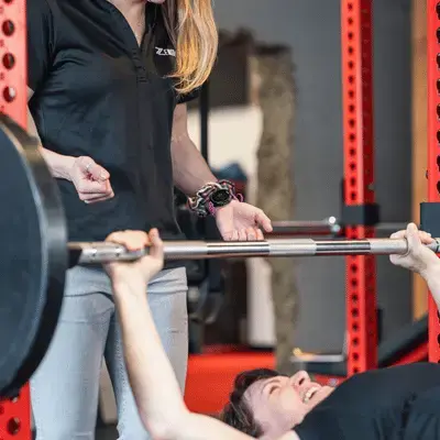 Trainer at Zenith Performance and Wellness spotting a client during a bench press session, emphasizing safe and consistent strength training for aging adults.