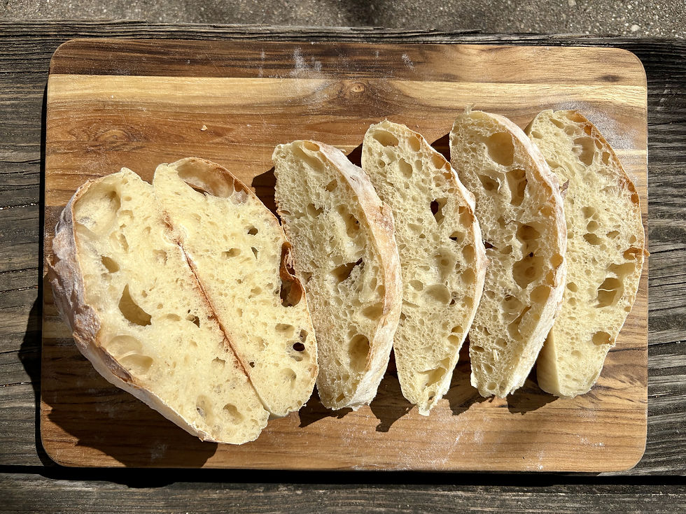 Slices of rustic bread with airy texture on a wooden board. Sunlit background with weathered wood creates a warm, rustic feel.