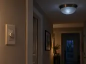Closed wall dimmer and ceiling LED fixture faintly glowing in a dark hallway