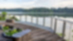 Nature Mandai Boardwalk Singapore. Wooden deck with benches and plants overlooks a calm lake bordered by lush trees under a cloudy sky, creating a serene atmosphere.