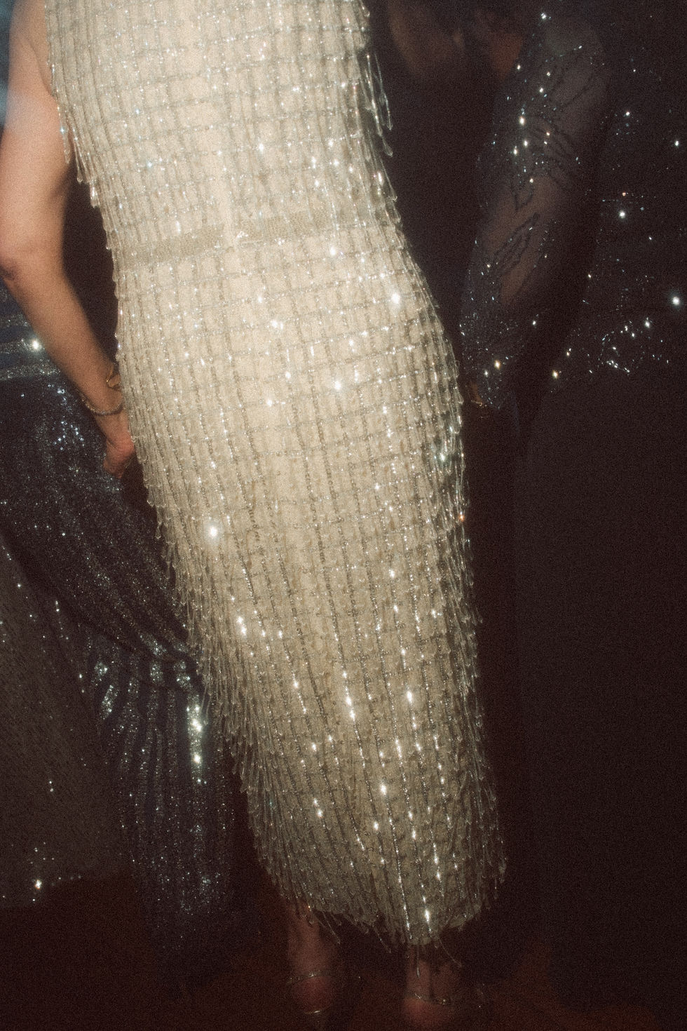 People in glittery dresses in a dimly lit setting, showcasing shimmering textures and patterns, creating an elegant and festive atmosphere.