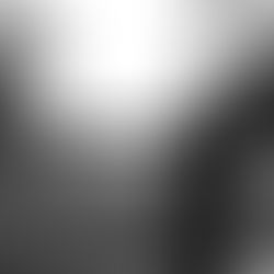 Person in a dark outfit and cowboy hat holds a camera in a grassy field. Trees in the background. Black and white image, mysterious mood.