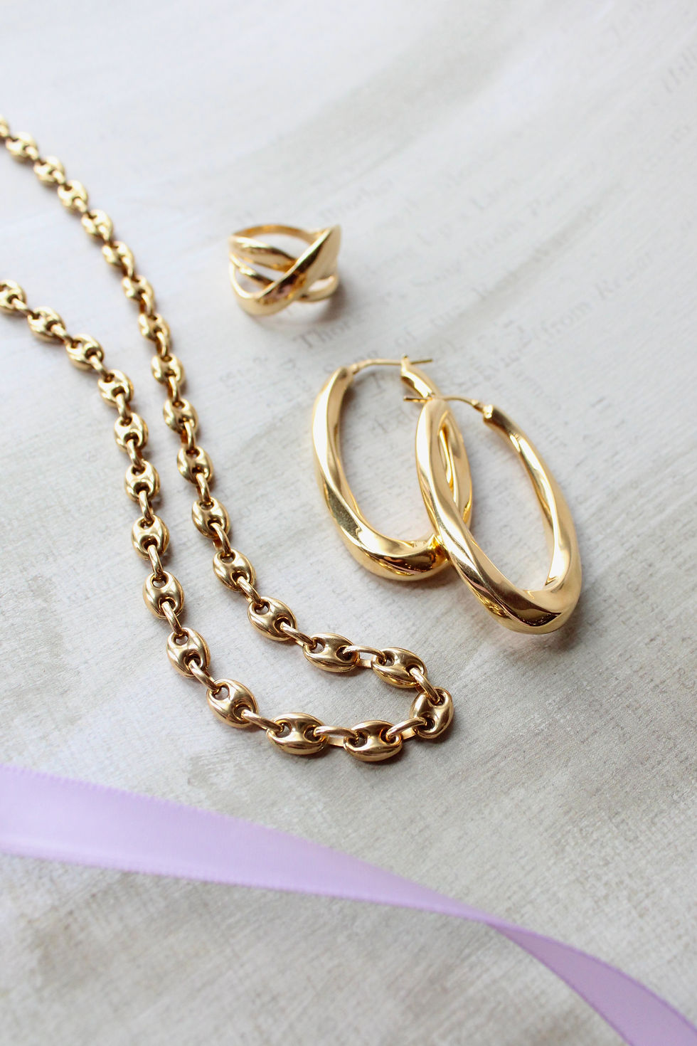 yellow gold jewellery flatlay; large oval gold earrings, crisis cross yellow gold ring, marine link yellow gold chain