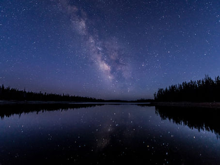 a starry night sky with the milky way visible over a mirroring lake.