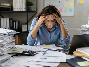 woman looking stressed and overwhelmed with large amount of financial documents scattered on her desk