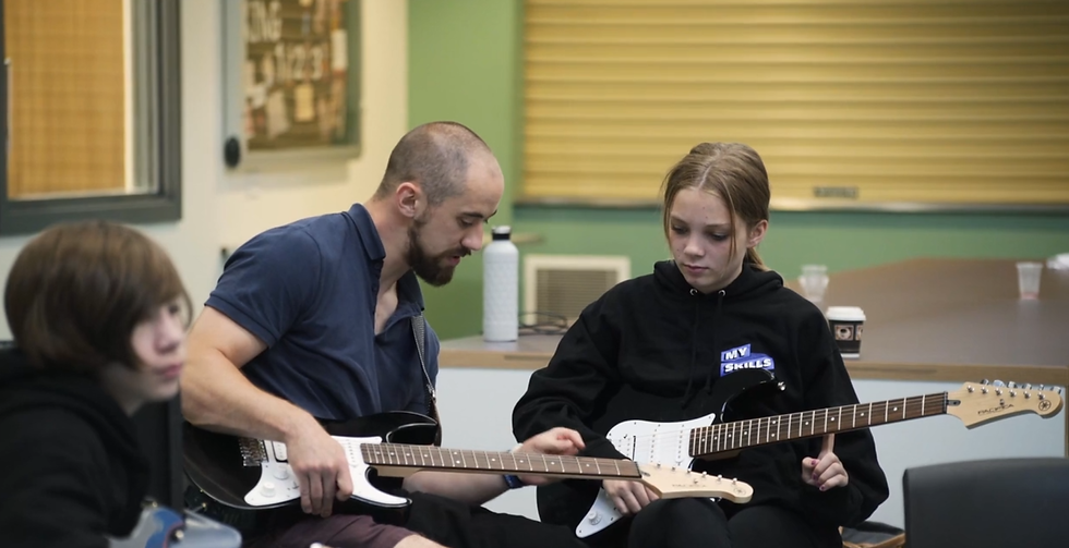 A teacher and two young people playing guitar