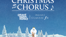 Snowman hugging a child in a snowy forest. Text: "The Big Christmas Chorus, Make Some Noise, Classic FM." Calm winter scene.