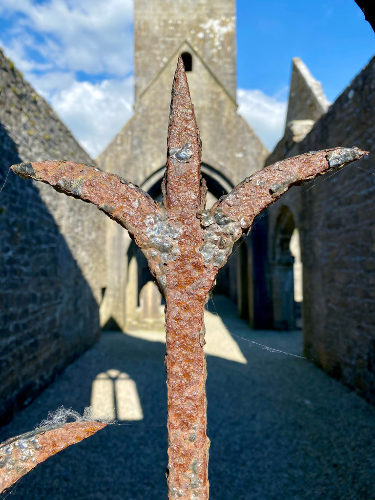 3 pointed rusted pole centered in front of a stone building and archway entrance