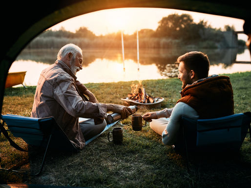 Father and son camping outdoors, pouring cups of coffee.