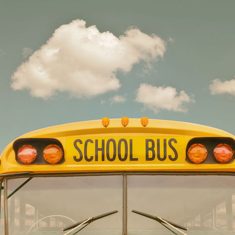 The front of an American school bus with a blue sky and a few clouds