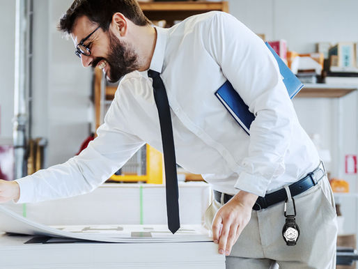 A young business man wearing a white dress shirt and a black tie looks at project plans with a Dakota Leather Clip attached to his khaki beltloop.