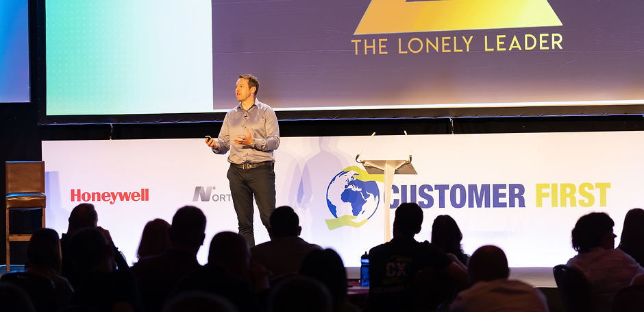 James Rule speaking on stage at a conference, a large Lonely Leader logo is on the screen behind