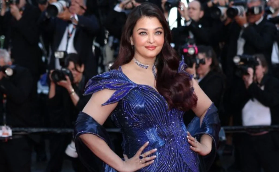 Woman in a shimmering blue gown poses on a red carpet, with photographers behind her in a glamorous, high-energy scene.