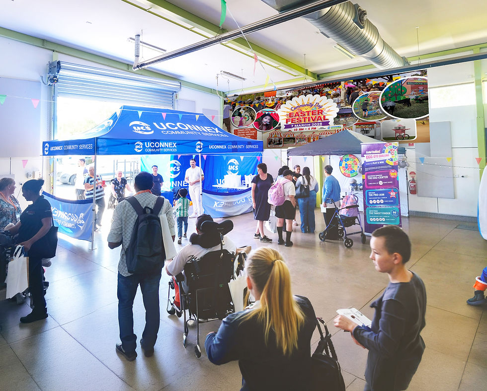 Wide-angle interior view of the bustling Shepparton community hall during the Easter Festival, featuring a blue Uconnex Community Services marquee, multiple activity stations