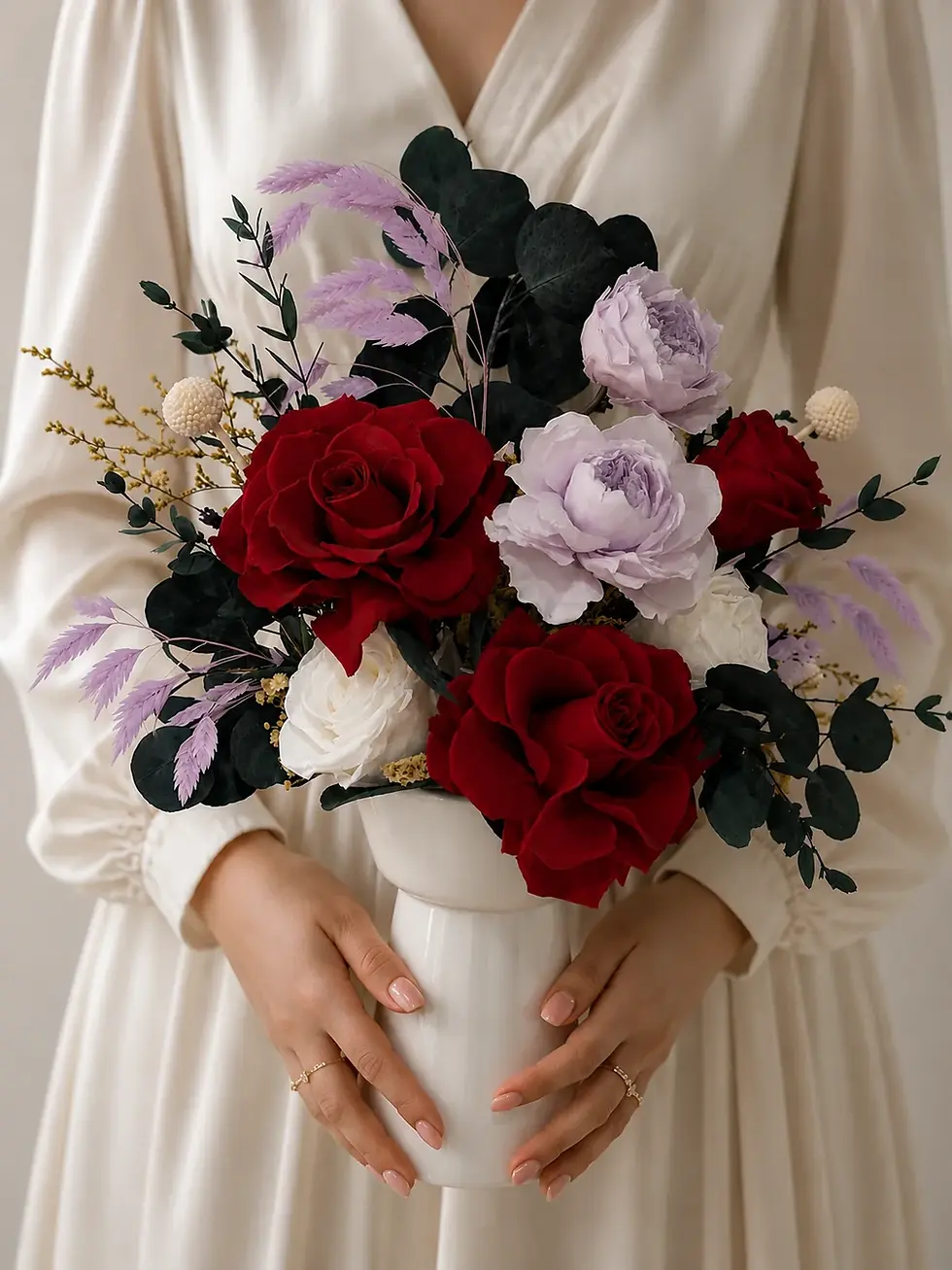 Woman holding the Amour arrangement with red roses, lavender and white blooms and dark eucalyptus in a white vase.