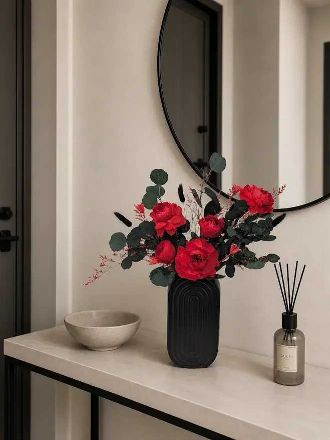 Ruby Garden Grace arrangement with red blooms and dark eucalyptus in a black vase on a hallway console.