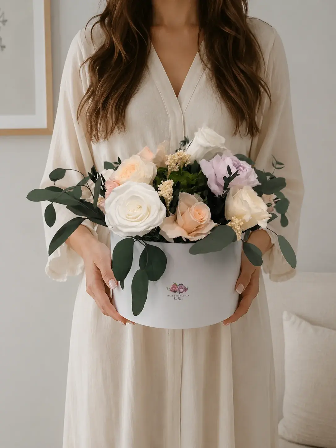 Woman holding Bloom, a white flower box filled with white, peach and lilac preserved roses and eucalyptus.