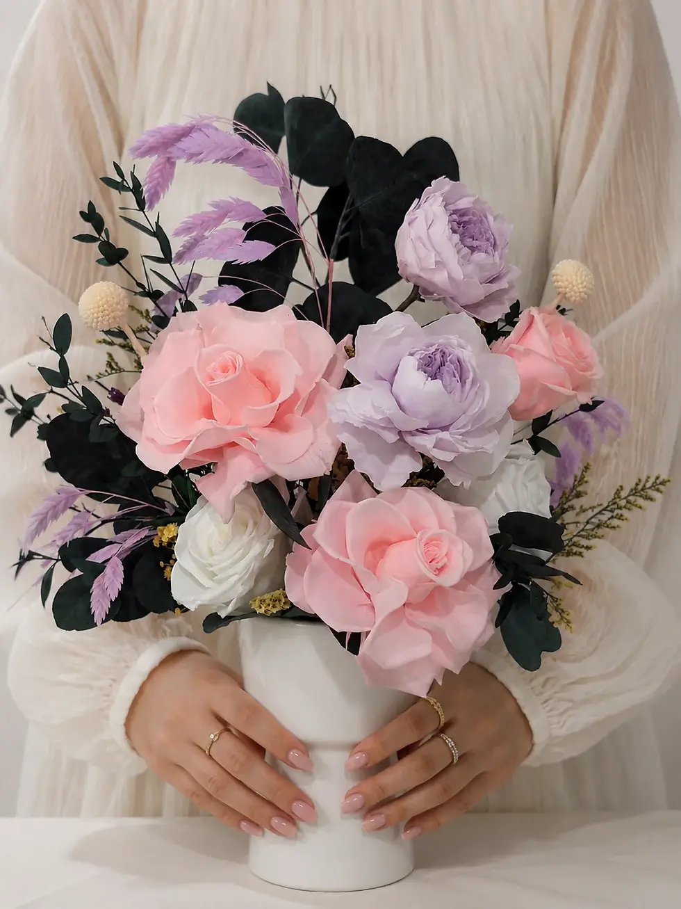Woman holding the Harmony arrangement with pink roses, lavender and white blooms and dark eucalyptus in a white vase.